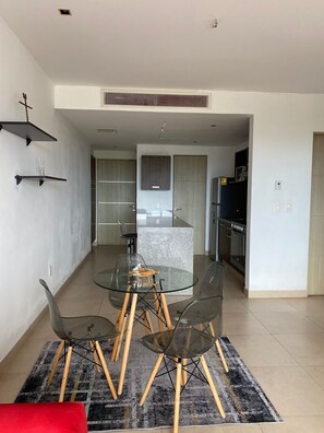 Eine moderne Küche mit einer zentralen Kochinsel, einem Essbereich mit Glastisch und Stühlen sowie einem roten Sofa.
