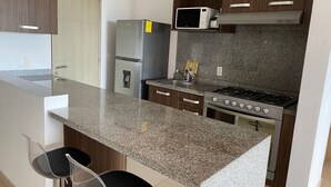 A modern kitchen with a granite countertop, stainless steel appliances, and wooden cabinets. - Apartment in Plaza las Americas tower Montevideo Cancun (Cancún)