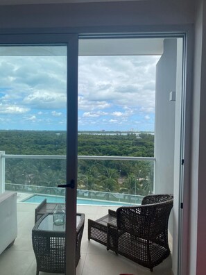 Ein Balkon mit Korbmöbeln, einem Glastisch und Blick auf einen Swimmingpool und Grünflächen.