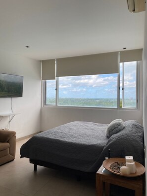 Ein Schlafzimmer mit Bett, Fernseher, Fenster mit Aussicht und Nachttisch mit Kerzen.