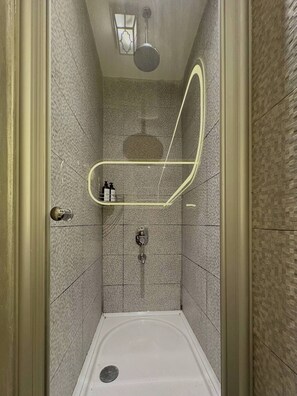 A small, tiled shower stall with a handheld showerhead, a wall-mounted faucet, and a light fixture above. - Taksim Square1 Bedroom Suite 05 (Istanbul)