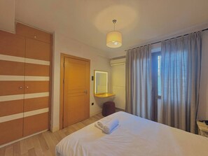 A hotel room with a bed, a wardrobe, a mirror, a bedside table, and a window with curtains. - Taksim Square1 Bedroom Suite 05 (Istanbul)