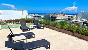 Eine Dachterrasse mit Liegestühlen, einem kleinen Tisch und Blick auf das Meer und die Stadt.