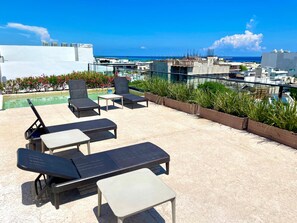 Eine Dachterrasse mit Liegestühlen, einem kleinen Tisch und Blick auf das Meer und die Stadt.
