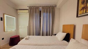 Ein Hotelzimmer mit zwei Betten, einem roten Pouf, einem großen Spiegel und einem Gemälde an der Wand.