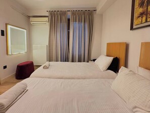 Ein Hotelzimmer mit zwei Betten, einem roten Pouf, einem großen Spiegel und einem Gemälde an der Wand.