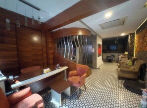 Ein modernes Interieur mit einer geschwungenen Holzwand, einer Sitzecke mit einer Bank und Sesseln, einem gemusterten Boden und einem Flachbildfernseher im Hintergrund.