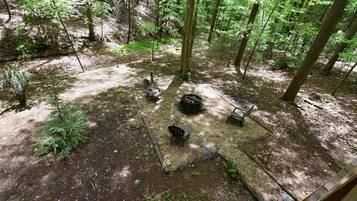 A forested area with a fire pit, benches, and a small table.