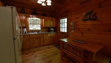 A wooden cabin interior with a kitchen, dining area, and a bear mural on the wall.