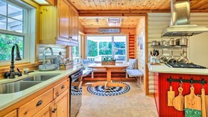 Une cuisine avec des meubles de rangement en bois, un évier, une cuisinière et une fenêtre donnant sur un espace verdoyant.