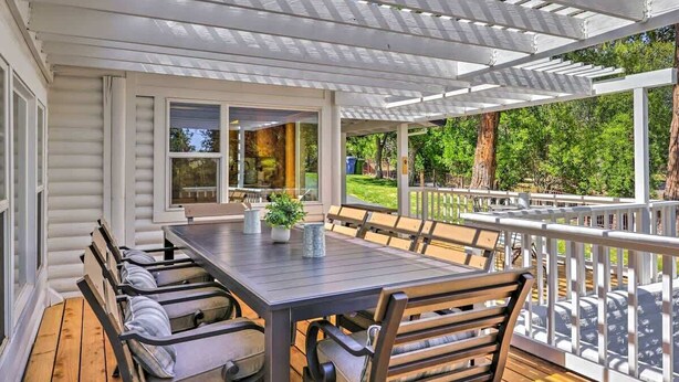 Une terrasse extérieure avec une table et des chaises en bois, une pergola et une vue sur la verdure environnante.