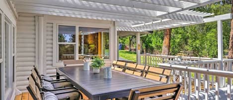 Un patio exterior con una mesa y sillas de madera, una pérgola y vistas al entorno verde.