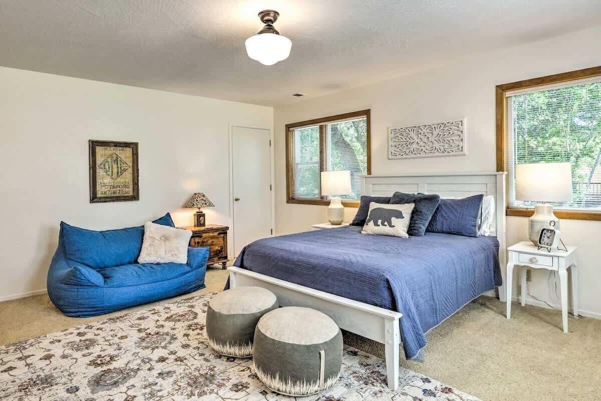 A bedroom with a bed, a blue sofa, two ottomans, a nightstand, a lamp, and a window with blinds.