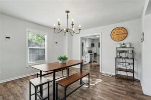 A dining area with a wooden table and benches, a chandelier, a clock, and a kitchen in the background. - Cozy Atlanta Home Minutes from Amphitheater, Downtown, Stadium & Attractions (Atlanta)