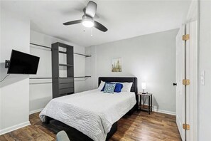 A bedroom with a bed, a ceiling fan, a TV mounted on the wall, a nightstand, and a door with a handle. - Cozy Atlanta Home Minutes from Amphitheater, Downtown, Stadium & Attractions (Atlanta)