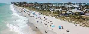 Ein Strand mit Menschen, Sonnenschirmen und Gebäuden im Hintergrund.