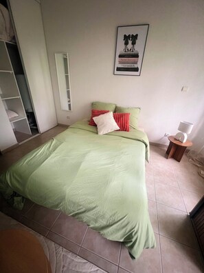 Un dormitorio con una cama, una mesita de noche con lámpara, un armario y un cuadro enmarcado en la pared.