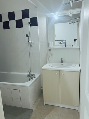 Un baño con bañera, lavamanos, espejo y toallero.