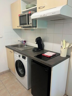 Una cocina compacta con lavadora, microondas, cafetera y escurreplatos.