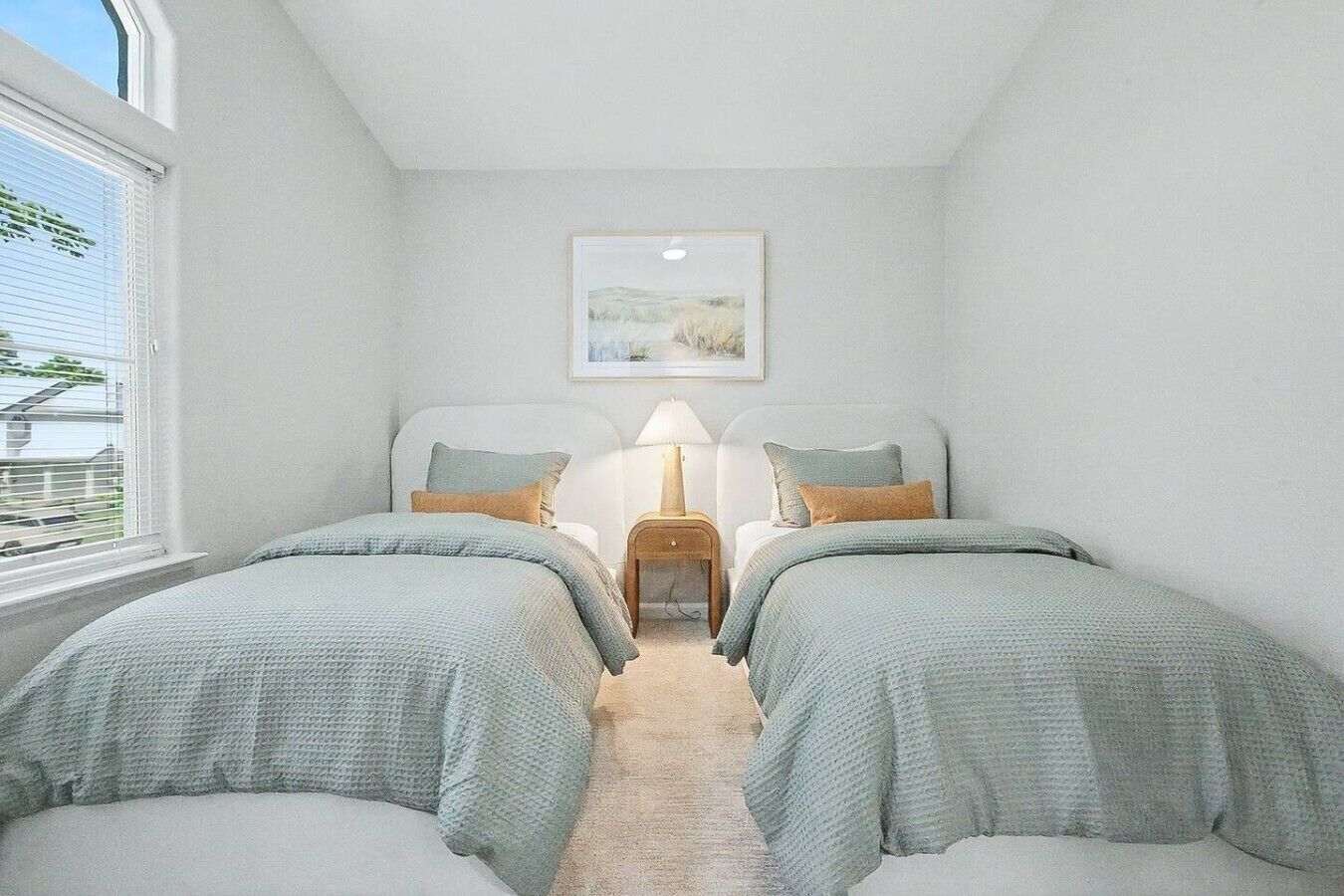 Een slaapkamer met twee bedden, een nachtkastje, een lamp en een lijst met een afbeelding aan de muur.