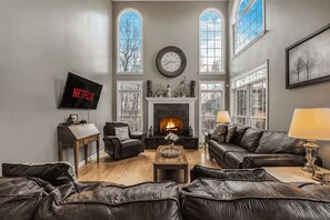 Ein Wohnzimmer mit Ledersofas, einem Kamin, einem Fernseher und großen Fenstern.