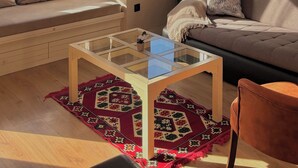A modern living room with a sofa, a glass coffee table, a patterned rug, and a view of the city through large windows. - Taksim Square1 Bedroom Suite 06 (Istanbul)