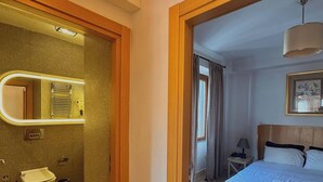 A hotel room with a bathroom, a bed, a bedside table, and a hanging light fixture. - Taksim Square1 Bedroom Suite 06 (Istanbul)