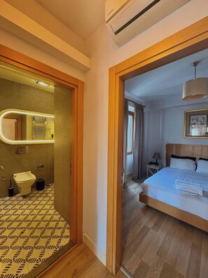 A hotel room with a bathroom, a bed, a bedside table, and a hanging light fixture. - Taksim Square1 Bedroom Suite 06 (Istanbul)