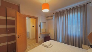 A hotel room with a bed, a wardrobe, a mirror, an air conditioning unit, and a window with curtains. - Taksim Square1 Bedroom Suite 06 (Istanbul)