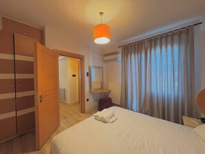 A hotel room with a bed, a wardrobe, a mirror, an air conditioning unit, and a window with curtains. - Taksim Square1 Bedroom Suite 06 (Istanbul)