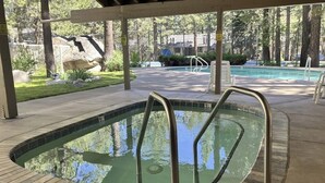 A swimming pool with a wooden deck, metal pool ladder, and a covered area with trees in the background. - Cozy Corner Condo with Shared Pool and Hot Tub, Close to the Lakes & Ski Resort (Mammoth Lakes)