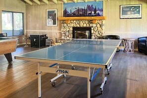 A ping pong table in a room with a stone fireplace, wooden walls, and a mountain painting. - 🏔 Cozy Mountain Condo in Mammoth Lakes | Sleeps 6 | Shared Hot Tub 🌲 (Mammoth Lakes)