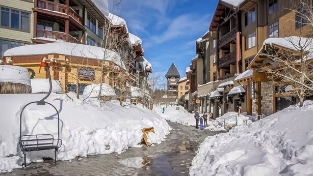 A snow-covered street with buildings, a bench, and a ski lift. - Ski-in/out condo with mountain view, private hot tub, deck & fireplace (Mammoth Lakes)