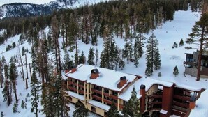 A multi-story lodge with a snow-covered roof, surrounded by a forested mountain area. - Ski-in/out condo with mountain view, private hot tub, deck & fireplace (Mammoth Lakes)
