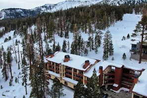 Ein mehrstöckiges Chalet mit schneebedecktem Dach, umgeben von bewaldeten Bergen.