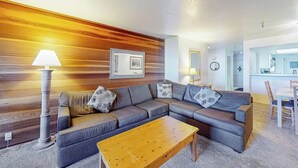 A living room with a sectional sofa, a wooden accent wall, a lamp, and a framed picture. - Ski-in/out condo with mountain view, private hot tub, deck & fireplace (Mammoth Lakes)