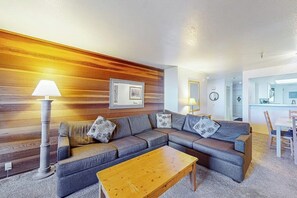 Ein Wohnzimmer mit Ecksofa, einer Wand aus Holzpaneelen, einer Lampe und einem gerahmten Bild.
