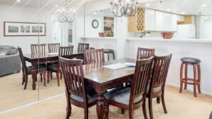 Un comedor con una mesa y sillas de madera, una araña y una cocina al fondo.