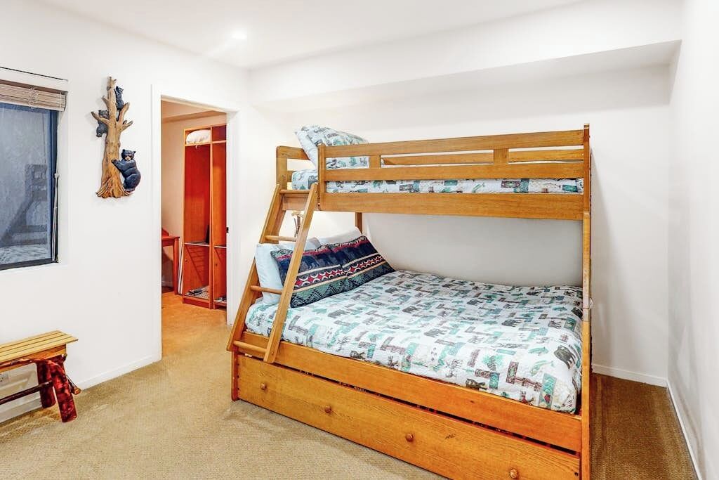 A bunk bed with a ladder, a wooden bench, and a wall-mounted decoration.