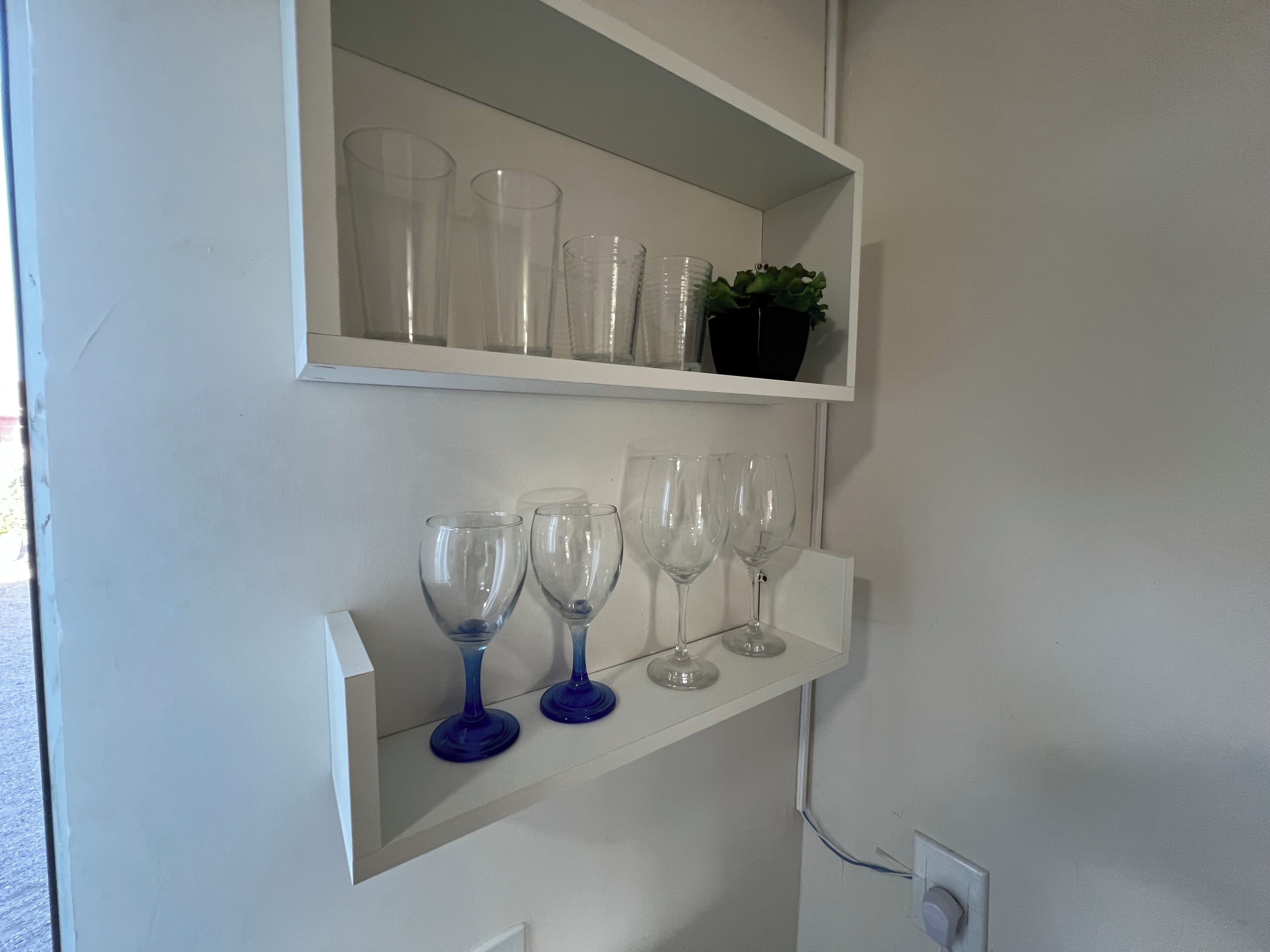 A white shelf with clear drinking glasses and a small potted plant.