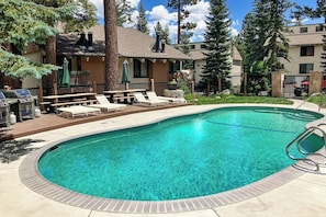 A swimming pool with lounge chairs, a barbecue area, and a building with a deck. - Delightful Dog-Friendly Condo with a Shared Pool, Sauna, and Hot Tub (Mammoth Lakes)