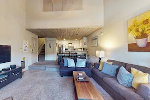 A modern living room with a sofa, coffee table, and a TV. A kitchen is visible in the background. - A Serene Destination with Shared Pool, Sauna, and Hot Tub (Mammoth Lakes)