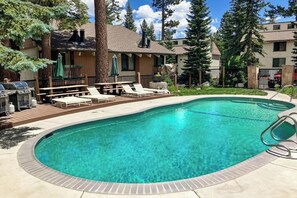 Ein Schwimmbecken mit Liegestühlen, einem Grill und einer Holzterrasse.