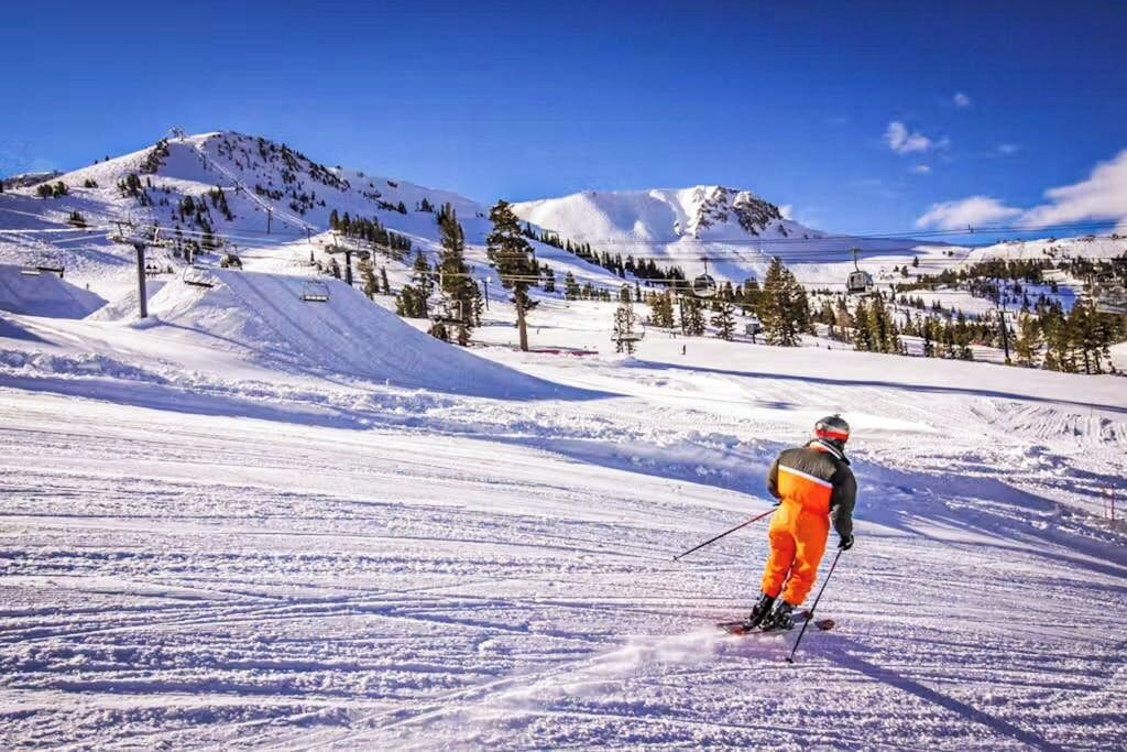 Une piste de ski avec un skieur, un télésiège et des montagnes enneigées.