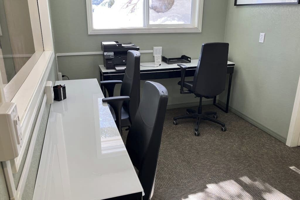 Ein Zimmer mit einem weißen Schreibtisch, schwarzen Bürostühlen, einem Drucker und einem Fenster mit Blick auf Schnee.