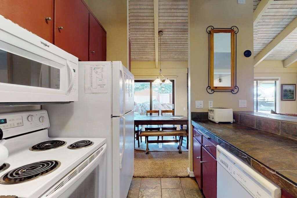 Una cocina equipada con estufa, microondas y refrigerador, junto a un comedor con mesa y sillas.