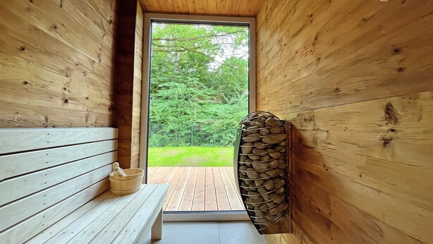 Interior de madera con un banco, una pared de piedra y vistas al exterior con vegetación.