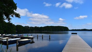 Un lago tranquilo con un muelle de madera que se adentra en el agua, rodeado de árboles y un cielo despejado.