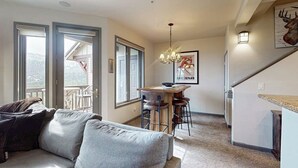 Ein Wohnzimmer mit einer Couch, einem Essbereich mit Tisch und Stühlen, einer Chandelüster und einer Küchenzeile mit Kühlschrank.