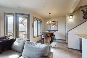 Ein Wohnzimmer mit einer Couch, einem Essbereich mit Tisch und Stühlen, einer Chandelüster und einer Küchenzeile mit Kühlschrank.